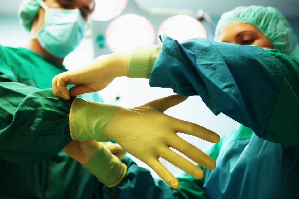 "Operating theatre staff wearing scrubs,one helping other put on gloves"