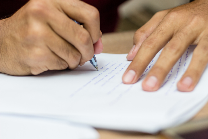A guy writing an essay with a pen on a paper