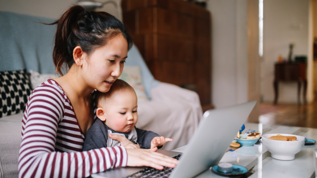 Asian mother and young baby sit in front of laptop working