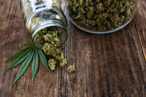 Cannabis bud pouring out of a glass jar on wood background