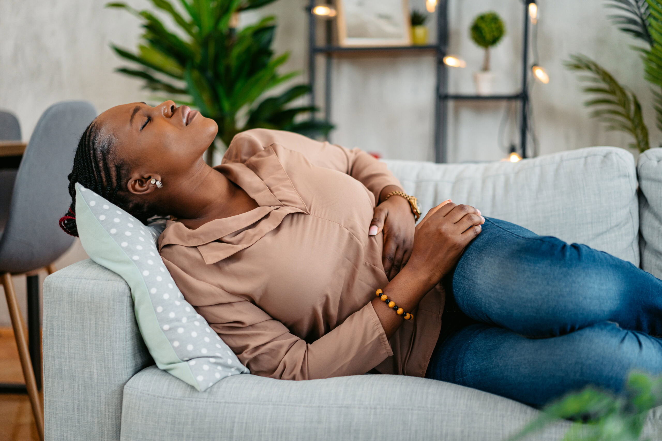 Young black woman lying on the sofa and having period cramps.