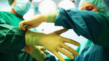 “Operating theatre staff wearing scrubs,one helping other put on gloves”