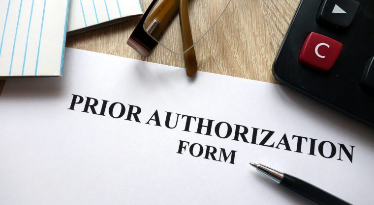 Prior authorization form with pen, calculator and glasses on desk