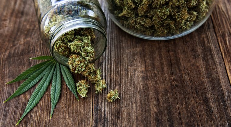 Cannabis bud pouring out of a glass jar on wood background