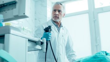 Calm mature medical worker standing with an endoscope and looking at the screen stock photo