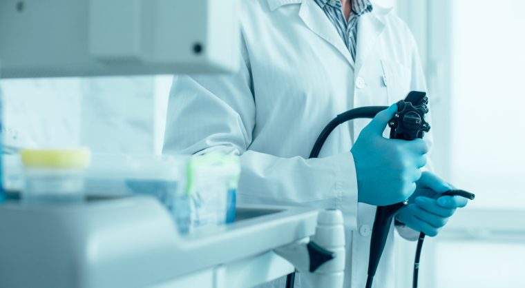 Cropped photo of a man in white coat and rubber gloves standing with a modern endoscope