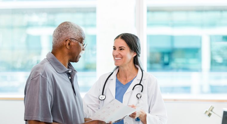 The mid adult female specialist smiles at her senior adult male patient as he asks a question about the information in the brochure.