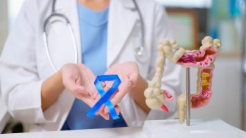 close up of female doctor hand wear white coat holds blue ribbon in front of her chest with colon model on table