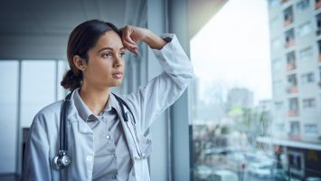 Shot of a young female doctor looking stressed out while standing at a window in a hospital