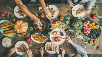 Flat-lay of friends feasting at Thanksgiving Day table with turkey Traditional Thanksgiving or Friendsgiving holiday celebration party. Flat-lay of friends or family feasting at Thanksgiving Day festive table with turkey, pumpkin pie, roasted seasonal vegetables and fruit, top view.