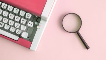 High angle view of retro typing machine and magnifier on table. Flat lay of vintage typewriter in red color and magnifying glass minimal creative concept.